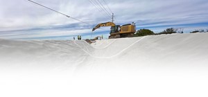 An image showing sections of deployed RCR® extending back from the foreground. A piece of CAT machinery in the center of the image is holding a roll of RCR®, and another piece of machinery is farther back in the image. People in yellow safety vests and hard hats are also shown. Powerlines are in the top of the image.